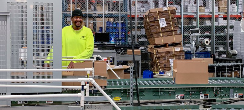 Smiling man in bright yellow working on conveyor belt line.