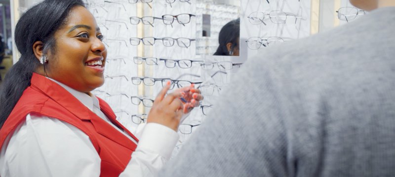 Smiling female African American National Vision employee helping a customer pick out new frames.