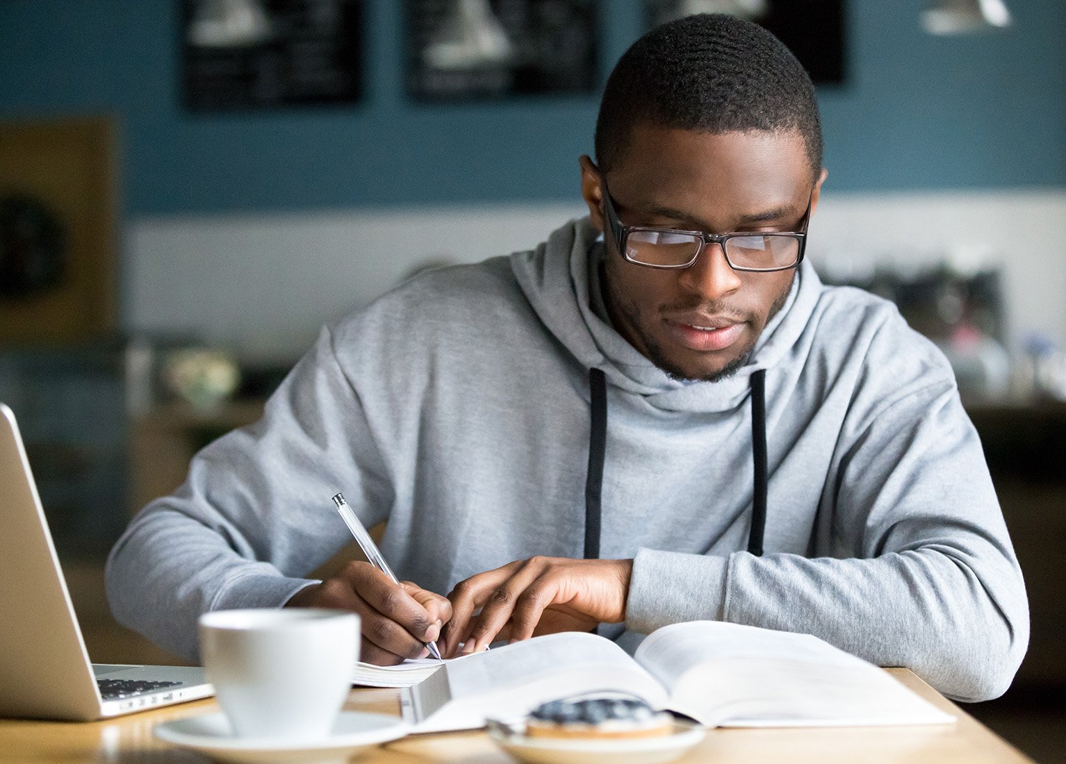 African American male wearing glasses and working on his studies at a coffee shop.